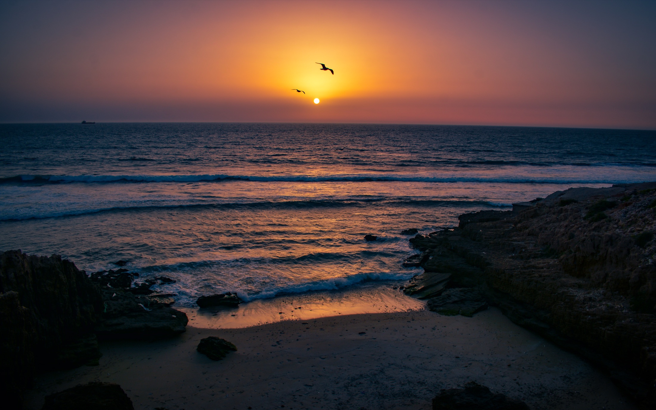 Lines of waves approaching a rocky coastline at sunset